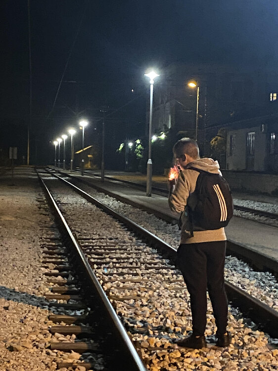 Could contain: clothing, track, outdoor, person, ground, sky, footwear, train, platform, standing, woman, night, railroad, light