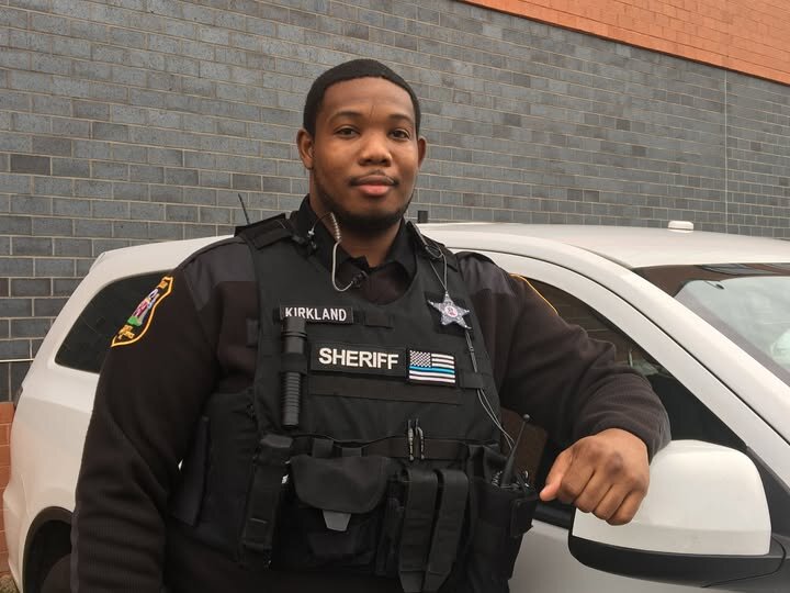 Could contain: person, clothing, vehicle, land vehicle, man, human face, law enforcement, car, outdoor, building, security, police officer, police, officer